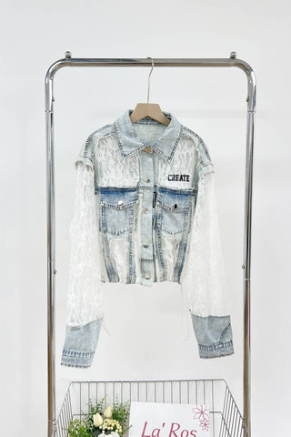 Denim jacket with lace overlay on a clothing rack against a white background