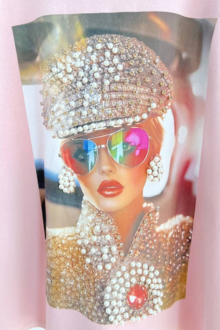 Person wearing a sparkling outfit with a hat and sunglasses on a pink background