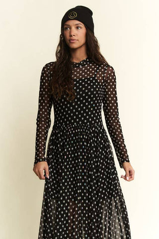 Woman wearing a black polka dot dress with long sleeves on a beige background