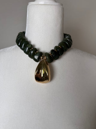 Olive green chunky beaded necklace with a large gold teardrop pendant on display bust.