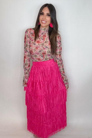 Woman wearing a floral top and pink fringe skirt against a white background