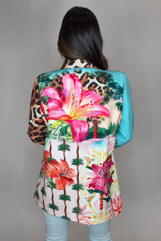 Person wearing a colorful floral and leopard print headscarf on a plain background