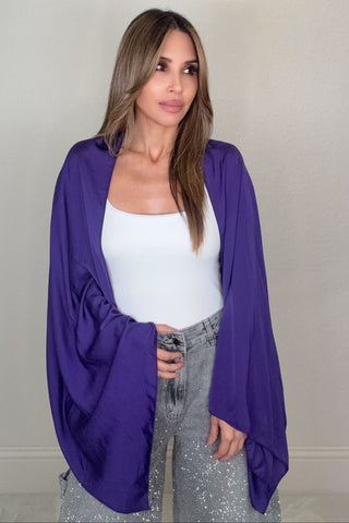 Woman wearing a violet open-front silk-style jacket with wide sleeves over a white tank and sparkly gray jeans.