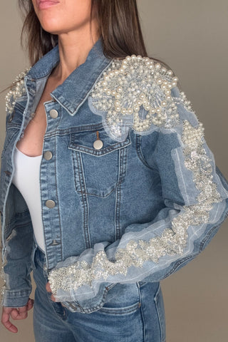 Denim jacket with pearl embellishments worn by a person against a neutral background