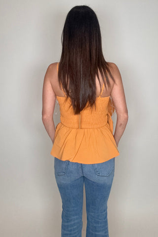 Person wearing an orange top and blue jeans on a plain background