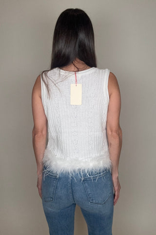 Person wearing a white sleeveless top and blue jeans against a plain background