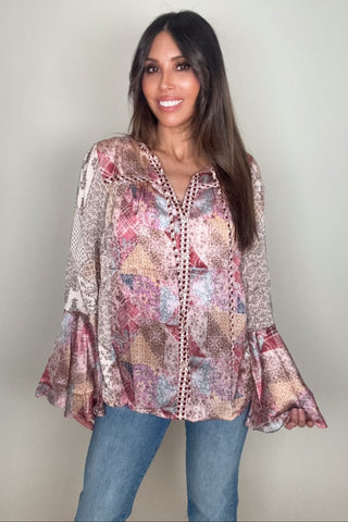 Woman wearing a patterned blouse and jeans against a plain background