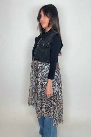 Woman wearing a black denim vest over a patterned dress with blue jeans on a white background