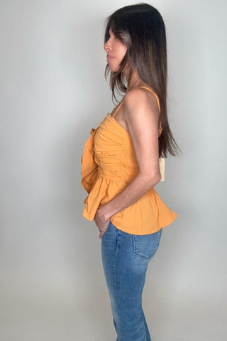 Woman wearing a mustard yellow top and blue jeans against a plain background