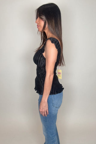 Woman wearing a black sleeveless top with a visible tag against a plain background