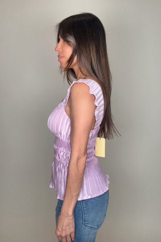 Woman wearing a purple sleeveless top with ruffled details against a plain background