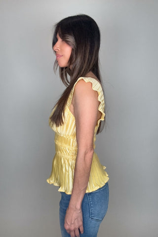 Woman wearing a yellow top and blue jeans against a gray background