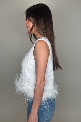 Woman wearing a white sleeveless top with feather details on a plain background