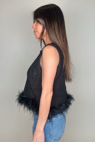Woman wearing a black sleeveless top with feather details on a plain background