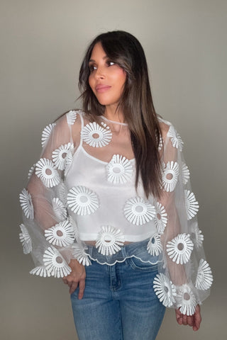 Woman wearing a white blouse with floral patterns and blue jeans against a neutral background