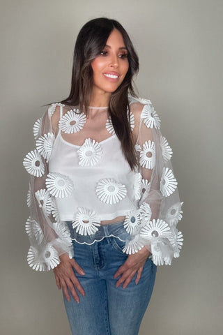 Woman wearing a sheer top with white floral embroidery against a plain background