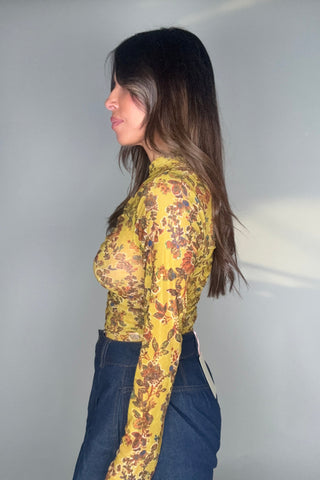 Person wearing a yellow floral jacket and blue jeans against a plain background