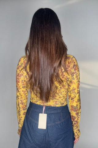 Person wearing a yellow floral top and blue jeans on a plain background