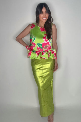 Woman wearing a green floral top and green skirt against a plain background