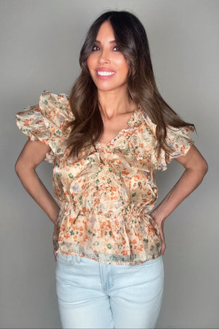 Woman wearing a floral blouse and light blue jeans against a gray background