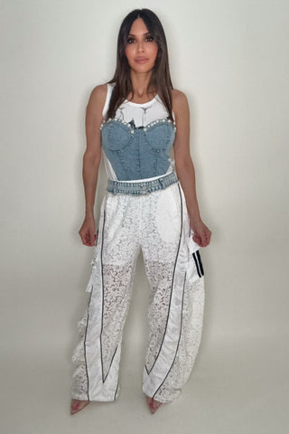 Woman wearing a denim corset top and white pants with black patterns on a plain background