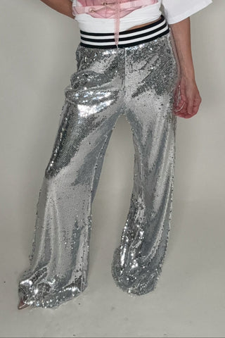 Person wearing a white t-shirt, pink top, and silver sequin pants on a plain background