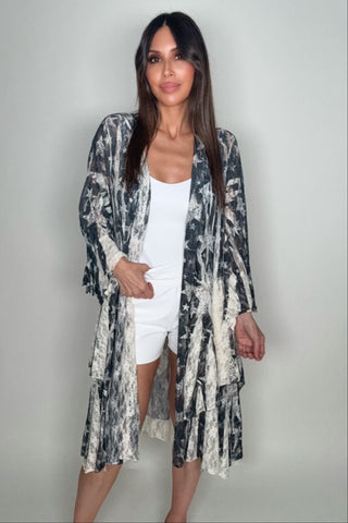 Woman wearing a long, patterned kimono over a white outfit on a plain background