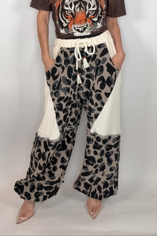 Woman wearing a brown t-shirt with a tiger design and leopard print pants on a white background