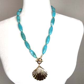 Turquoise beaded necklace with a gold-tone shell pendant and lobster claw clasp, styled as a coastal statement accessory.