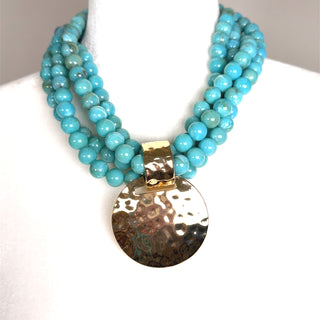 Layered gold necklace with turquoise beads and a hammered gold disc pendant featuring a turquoise center stone.