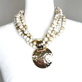 Beige beaded layered necklace with three strands of marbled beads and a hammered gold-tone disc pendant.