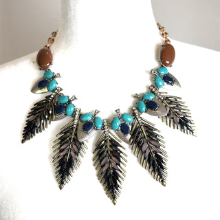 Turquoise and navy gemstone feather statement necklace with metallic accents and oversized leaf pendants displayed on a white bust.