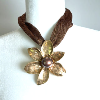 Brown metallic and gold floral pendant necklace with a dimensional sculpted flower, textured petals, center orb accent, and wide ribbon choker.