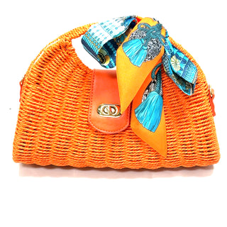 Orange woven straw handbag with a structured shape, printed scarf detail, adjustable strap, and secure flap closure.