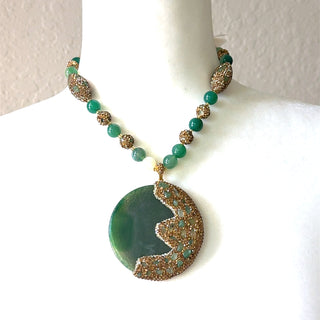 Green gemstone pendant necklace with a large round pendant, gold crystal detailing, faceted beads, and an adjustable gold chain.