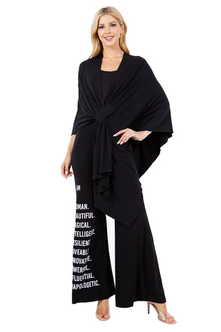 Black wrap-style shawl with bold white I Am Woman script, shown as a statement layering accessory.
