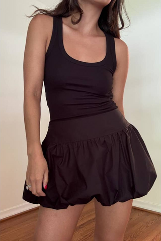Person wearing a black tank top and skirt indoors.
