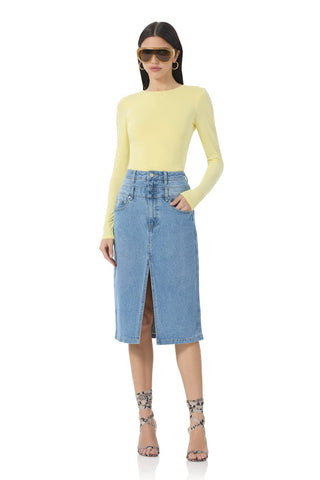 Woman wearing a yellow long-sleeve top and blue denim skirt on a white background