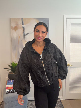 Black cropped zip-front hooded jacket with tonal floral texture, drawstring hood, elastic hem, and long balloon sleeves.