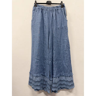 Chambray blue wide leg palazzo pants with lace trim at the hem hanging on a hanger against a neutral wall.