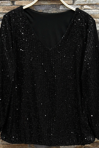Black sequin top on a hanger against a stone wall background