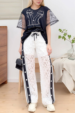 Person wearing a navy top with sheer sleeves and white lace pants in a room setting.