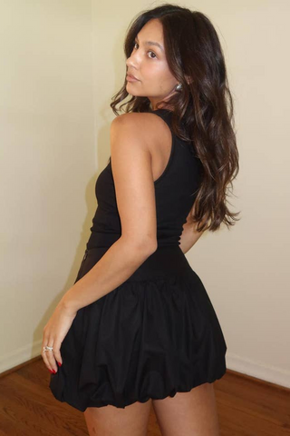 Woman wearing a black dress against a plain wall.