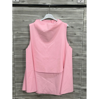 Back view of a blush pink sleeveless layered swing top on a hanger against a wood background.