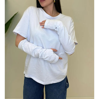 Woman wearing a clean white knit top with layered long sleeves and blue jeans.