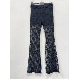 Black floral lace sheer flare pants with dramatic bell bottom silhouette hanging on a hanger against a white wall.