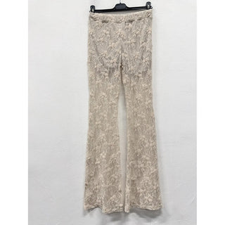 Ivory sheer floral lace flare pants with a vintage-inspired silhouette hanging against a white wall.